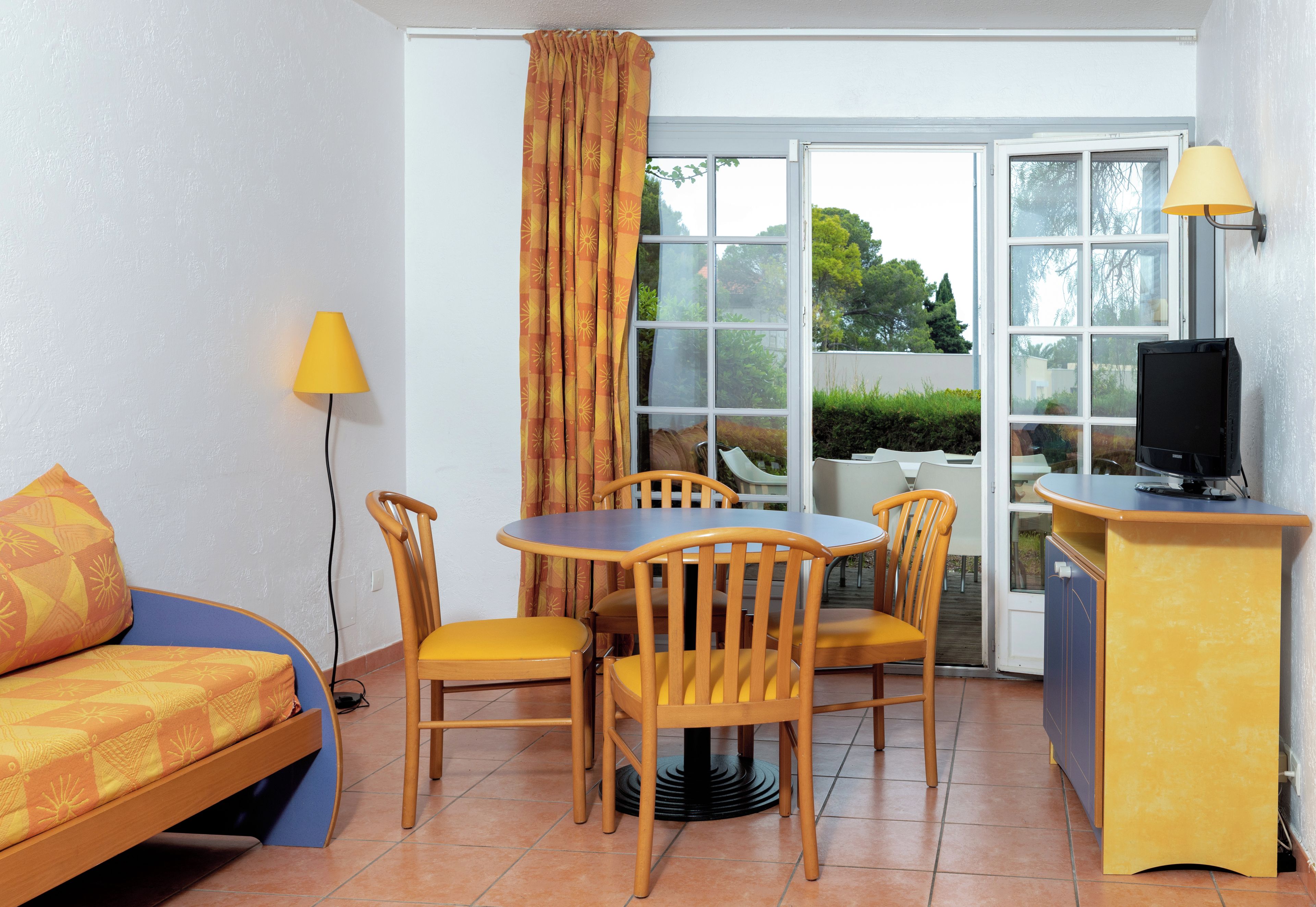 Una habitación compacta con cama, una mesa de comedor con sillas, un televisor y una lámpara.