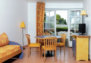 A compact room with a bed, a dining table with chairs, a TV, and a lamp.