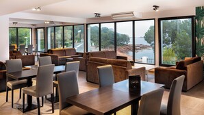 A modern lounge area with sofas, tables, and chairs, large windows offering a view of the outdoors.