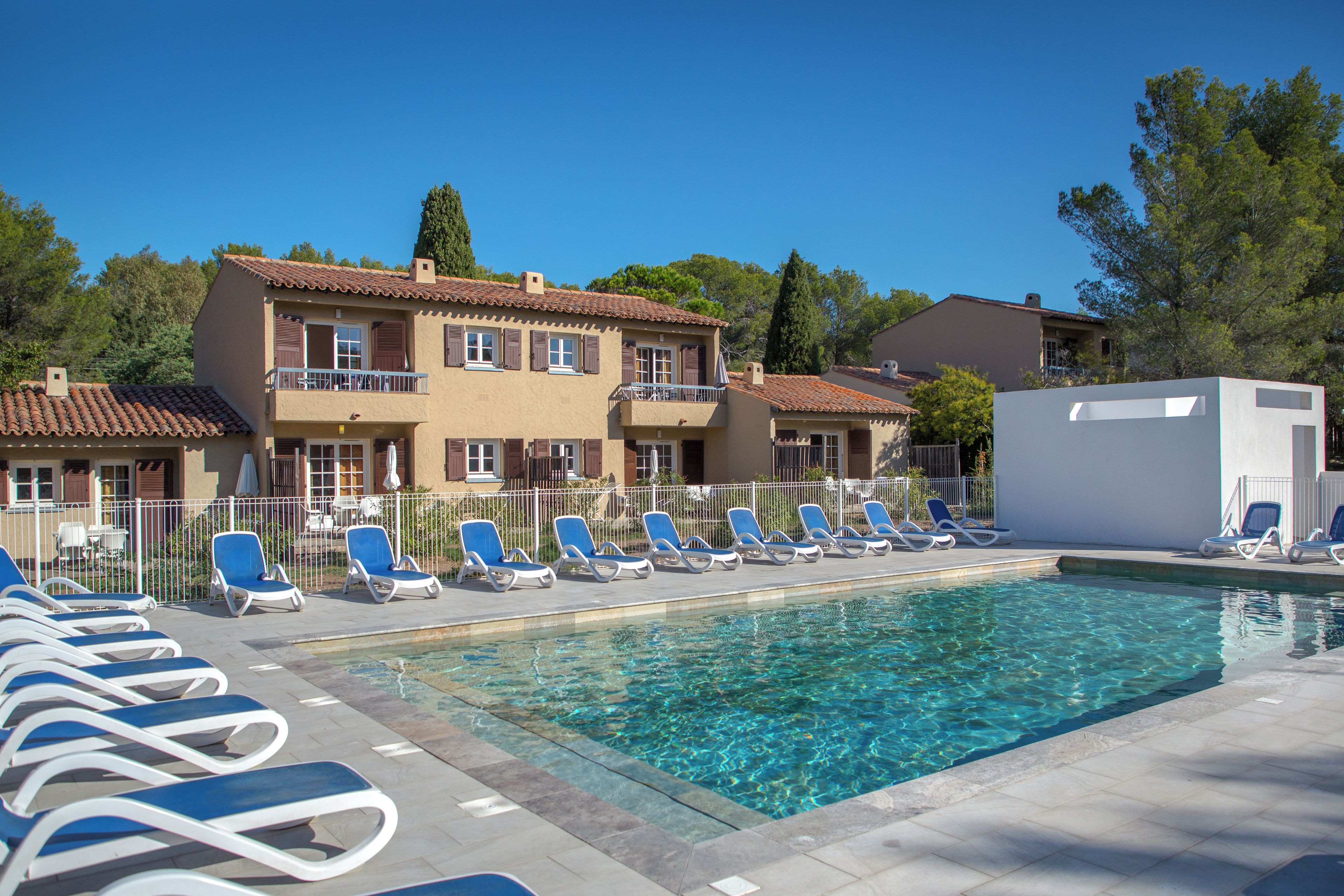 A swimming pool with lounge chairs and a building with multiple balconies.