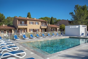 A swimming pool with lounge chairs and a building with multiple balconies. - Sowell Residences Les Chenes Verts (Saint-Raphael)