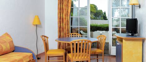 Ein kleines Zimmer mit einem Bett, einem Esstisch mit Stühlen, einem Fernseher und einer Lampe.