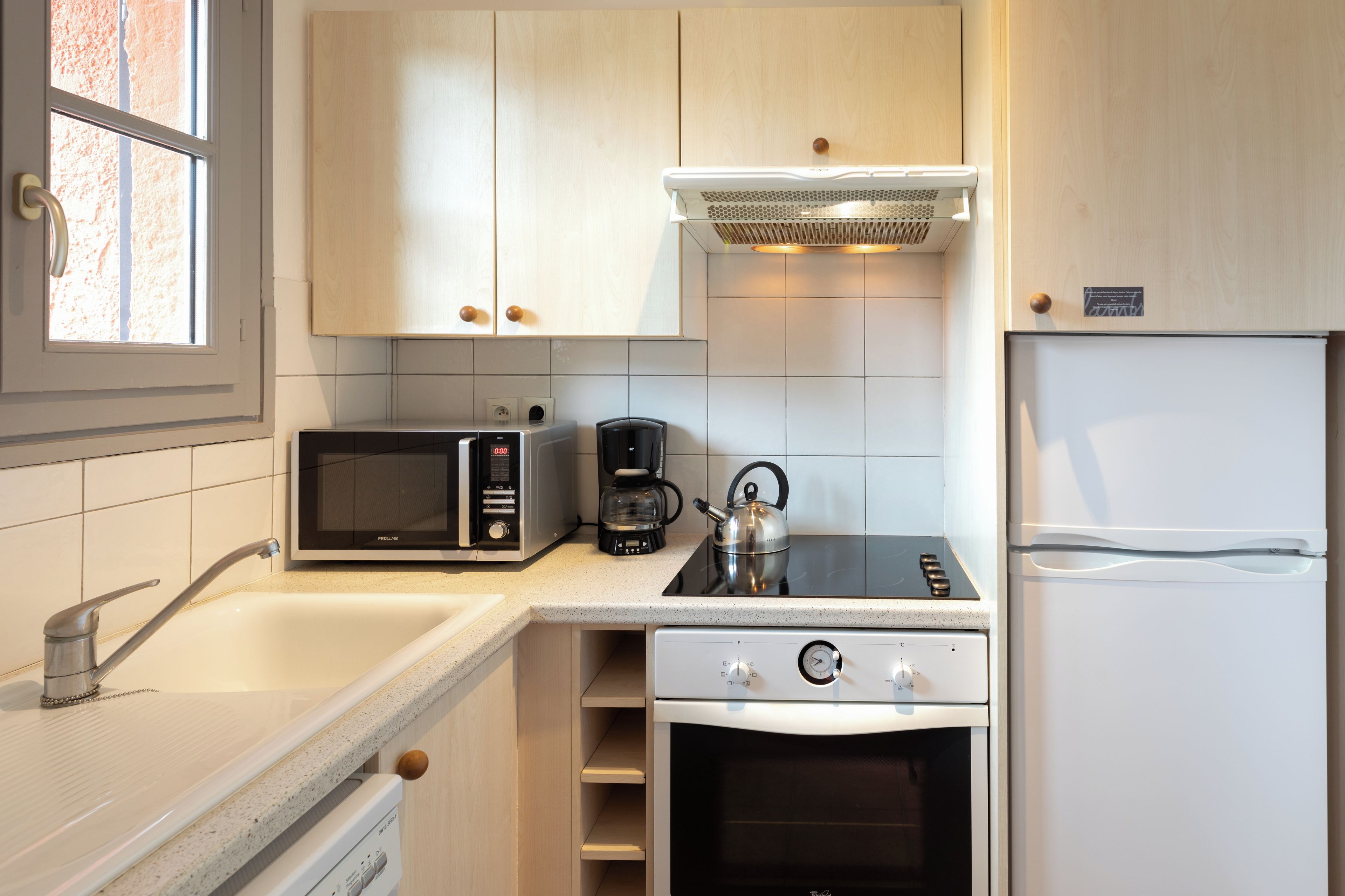 A compact kitchen with a microwave, coffee maker, kettle, and a refrigerator.