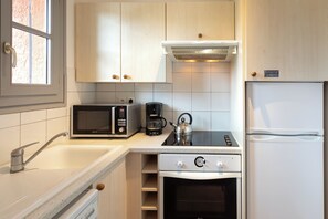 A compact kitchen with a microwave, coffee maker, kettle, and a refrigerator.