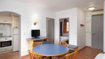 Una habitación de hotel compacta con cocina, una mesa de comedor con sillas, una cama y un televisor.