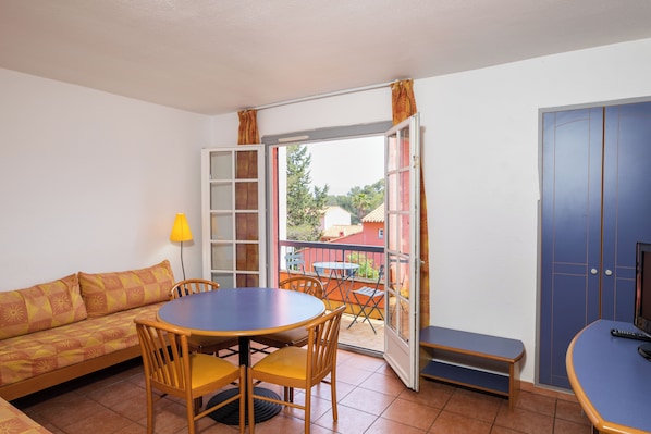 A room with a sofa, a round table with chairs, a bench, and a TV. - Sowell Residences Les Chenes Verts (Saint-Raphael)