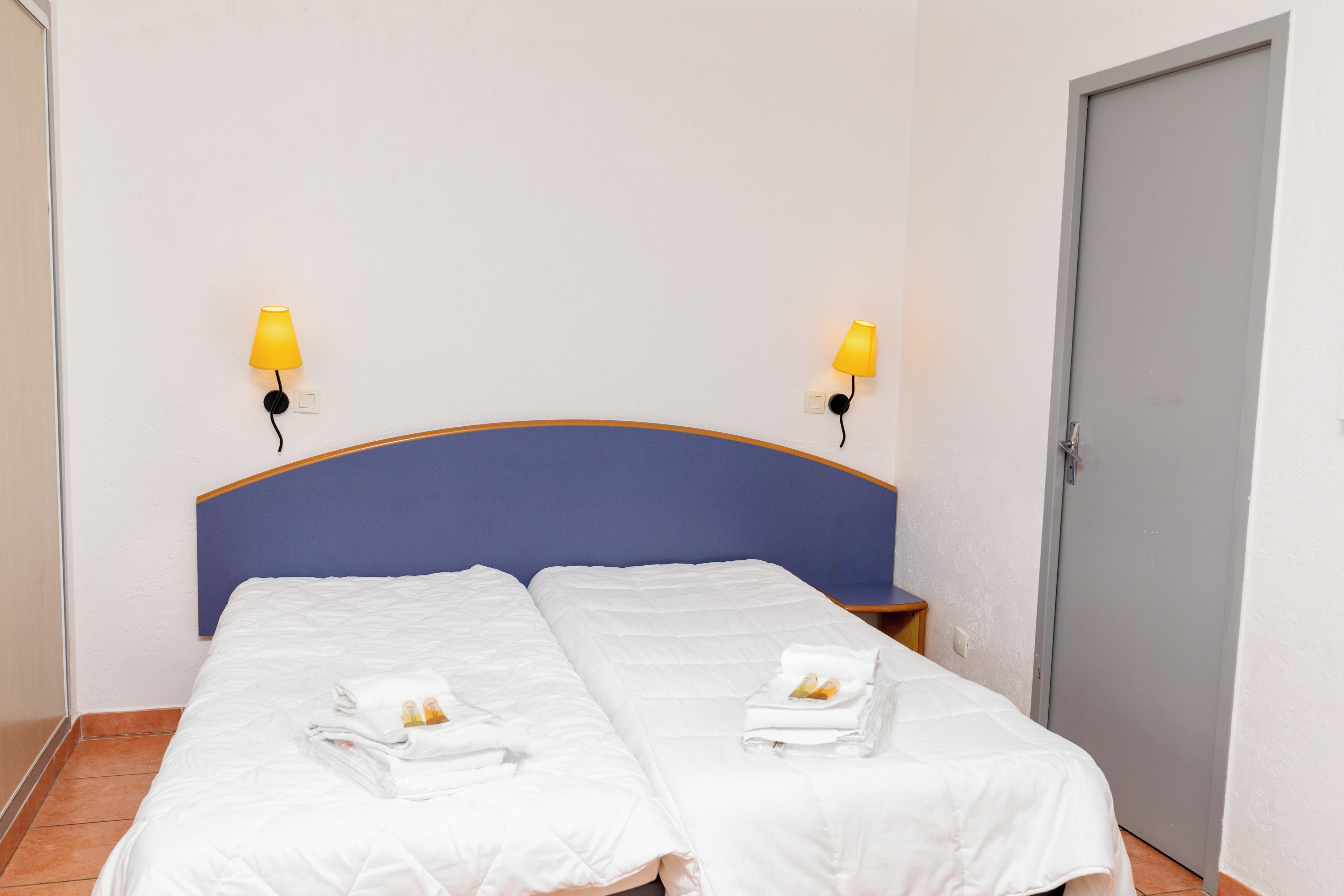 Et hotelværelse med to senge, en blå sengegavl og to væglamper.