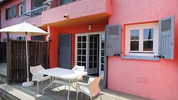 Un edificio rosa con balcón, una mesa blanca con sillas y una terraza de madera.