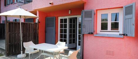 A pink building with a balcony, a white table with chairs, and a wooden deck.