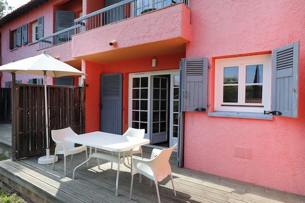 A pink building with a balcony, a white table with chairs, and a wooden deck.
