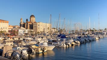 A marina with numerous boats docked, a prominent building with domed architecture, and a clear blue sky.