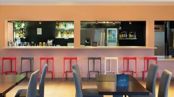 A bar area with a counter, shelves of beverages, and a refrigerator. There are multiple chairs and tables arranged for seating.