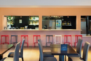 Zona de bar con mostrador, estantes llenos de bebidas y un refrigerador. Hay varias sillas y mesas dispuestas para sentarse.