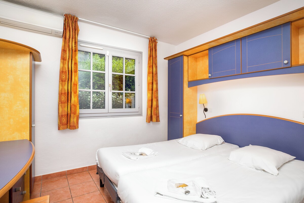 A hotel room with a bed, a desk, a window with curtains, and a blue headboard.