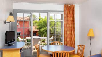 Una habitación con televisión, una mesa, sillas y una ventana con cortinas.