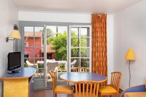 A room with a TV, a table, chairs, and a window with curtains. - Sowell Residences Les Chenes Verts (Saint-Raphael)
