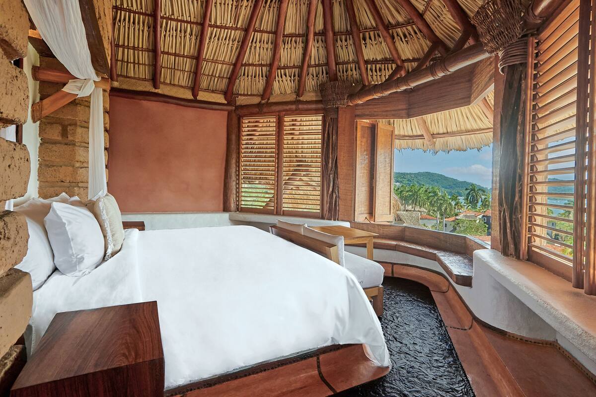 Een kamer met een bed, een klein tafeltje en een bank bij een raam met uitzicht op een berg en palmbomen.