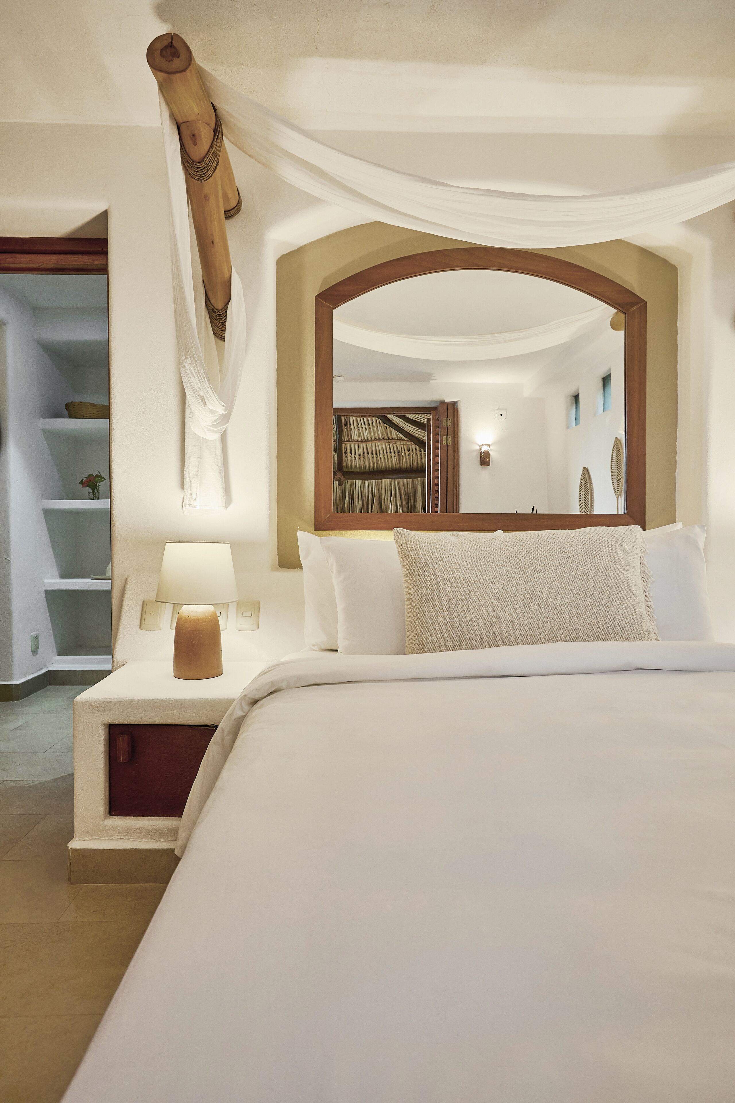 Un dormitorio ordenado con una cama grande, una mesita de noche con lámpara y un espejo sobre la cama.