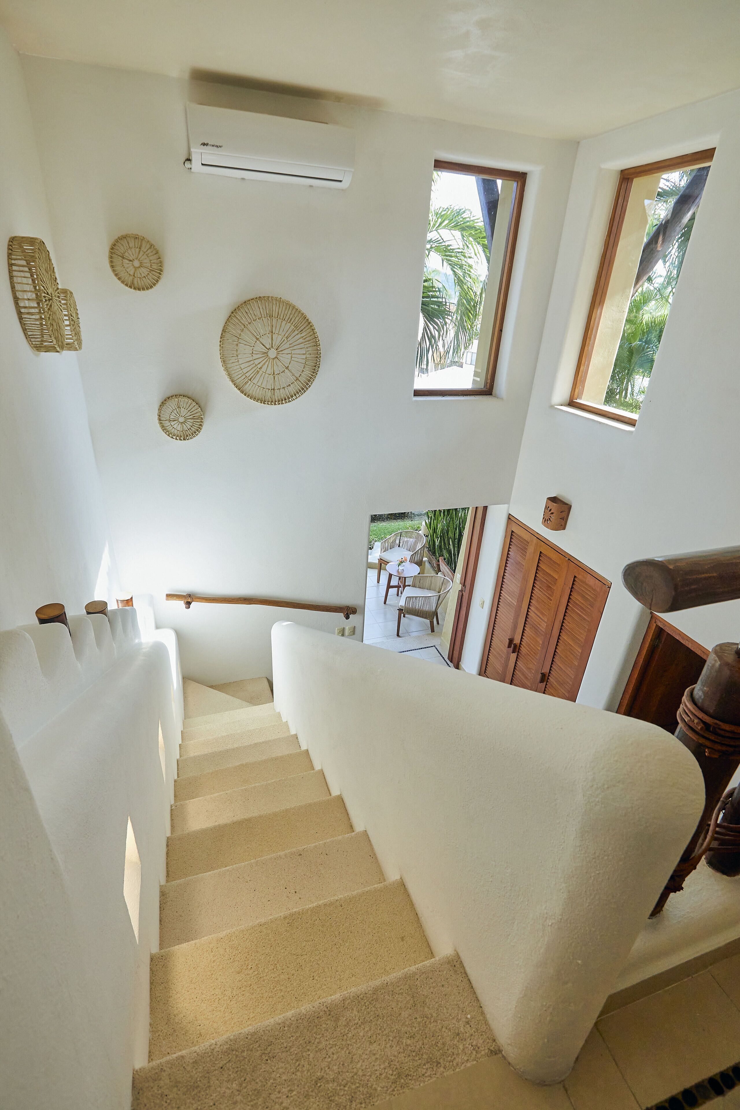 Una escalera con barandilla acolchada blanca, una puerta de madera y vista a un patio exterior con sillas y una mesa.