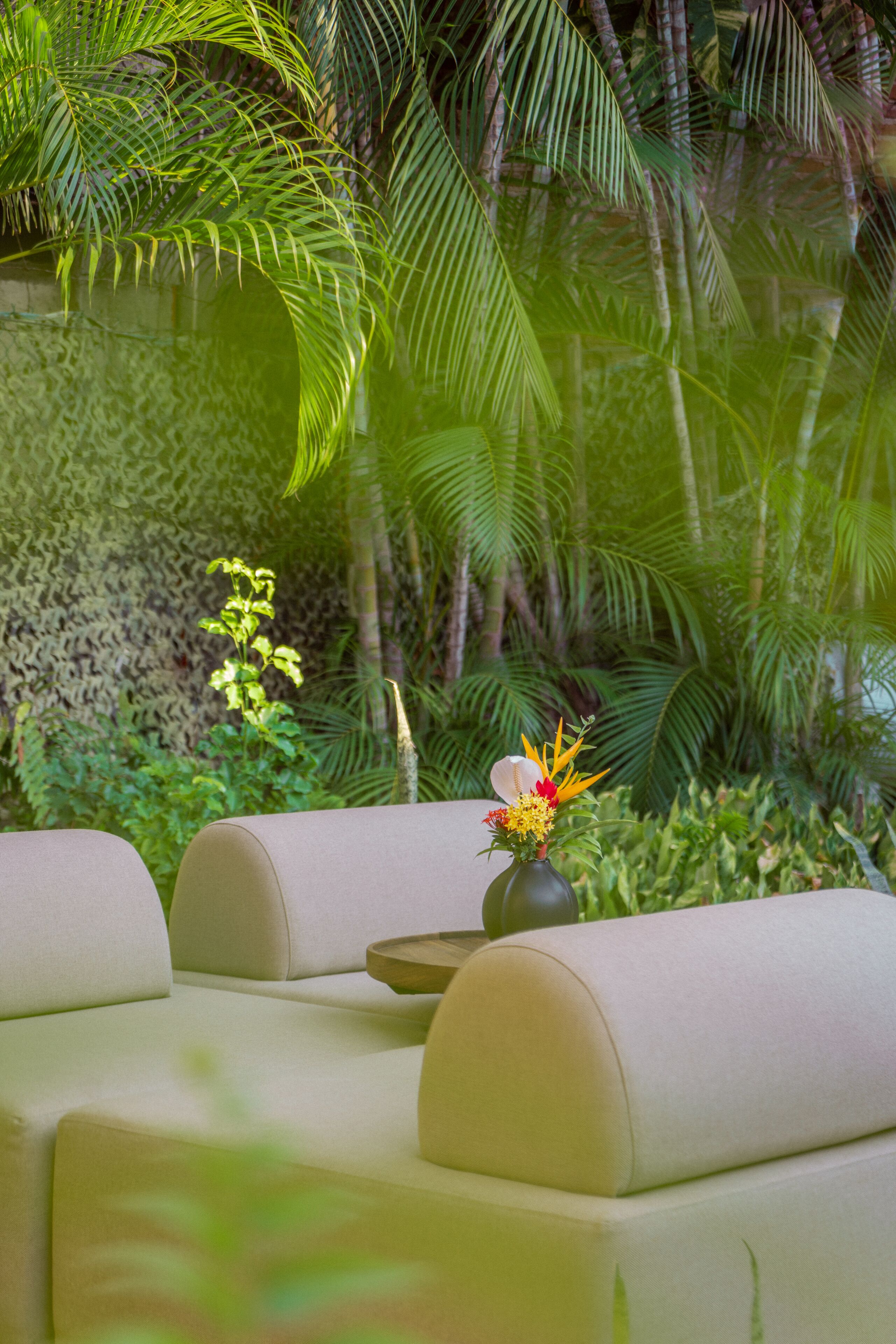 A seating area with a vase of flowers and a small table, surrounded by lush greenery and palm trees.