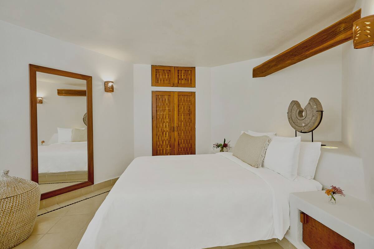 Een slaapkamer met een groot bed, een houten hoofdbord, een spiegel en een nachtkastje met een bloevas.