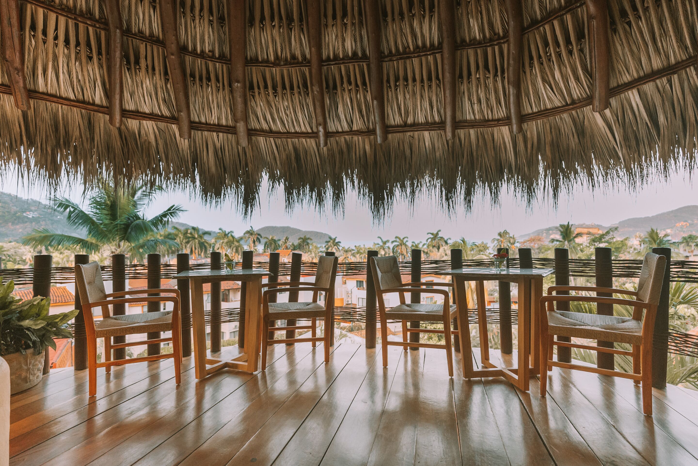 Un espace extérieur abrité, doté de tables et de chaises en bois, offrant une vue sur un paysage montagneux.