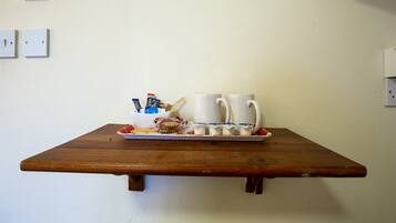A wooden table with a tray holding two white mugs, a bowl with snacks, and packaged food items.