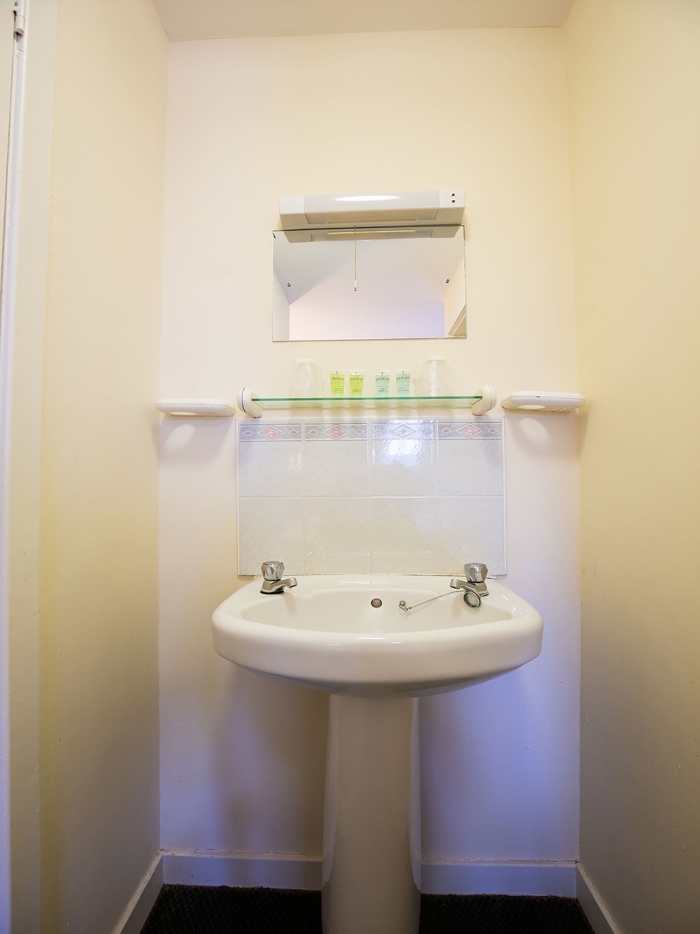 A bathroom with a pedestal sink, a mirror above it, and a shelf with toiletries.