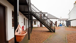 Ein Innenhof mit einem Ziegelpflasterweg, einer schwarzen Metalltreppe und einem weißen Gebäude mit zahlreichen Fenstern und Türen.
