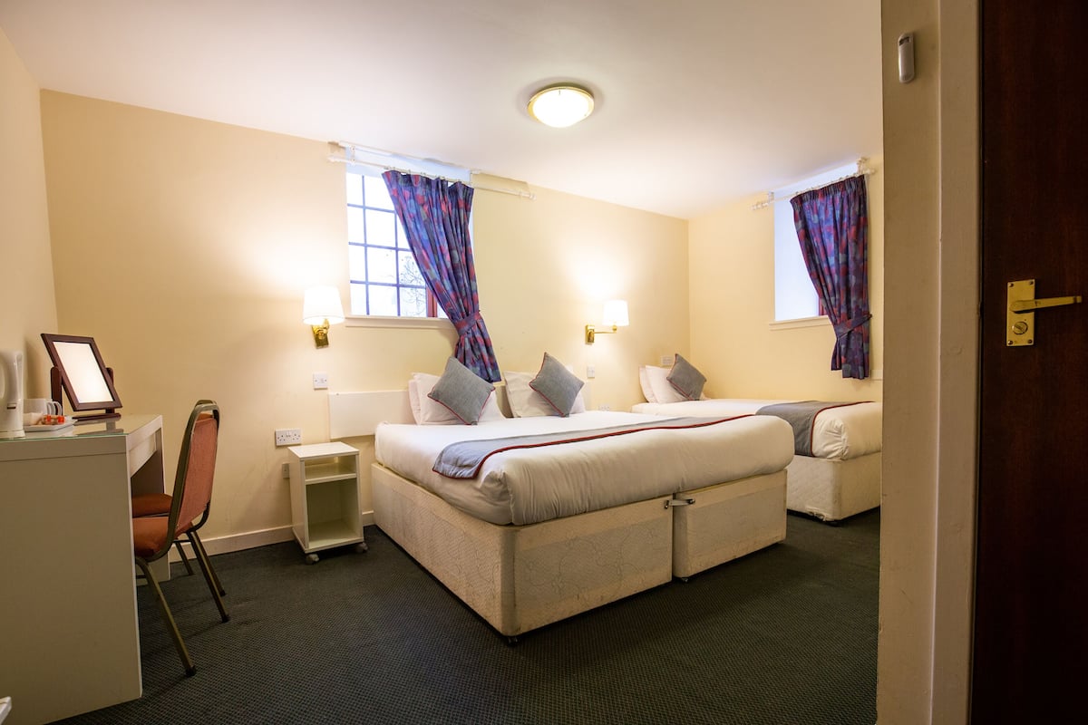 A hotel room with a bed, a desk, a chair, a nightstand, and a window with curtains.