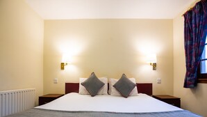 Ein Hotelzimmer mit einem großen Bett, zwei Nachttischen, zwei Wandlampen, einem Fenster mit Vorhängen und einer Heizung.