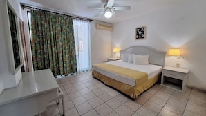 A hotel room with a bed, two bedside tables with lamps, a ceiling fan, a window with curtains, and a desk. - Hotel Costa Brava (Manzanillo)