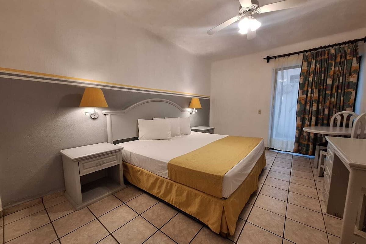 Una habitación de hotel con cama, mesitas de noche, un escritorio y un ventilador de techo.