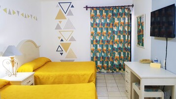 Una habitación con dos camas, un escritorio, una silla, una lámpara, un televisor y una cortina estampada.