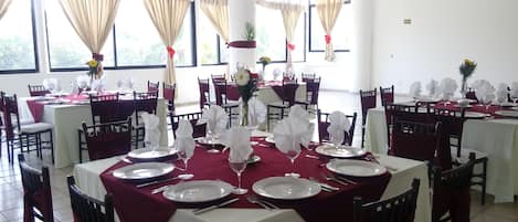 Comedor con mesas dispuestas para una comida, con manteles blancos y servilletas rojas.