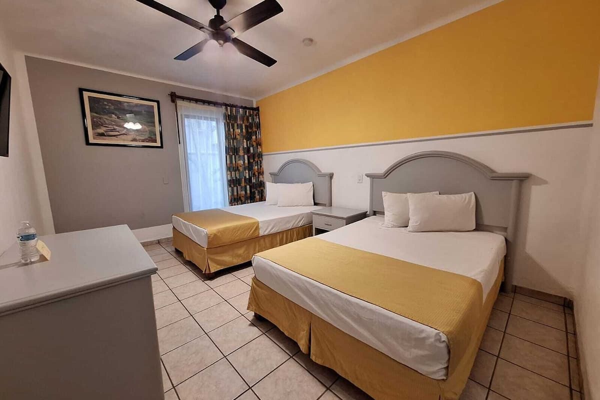 Una habitación de hotel con dos camas, un escritorio, un ventilador de techo y una ventana con cortinas.