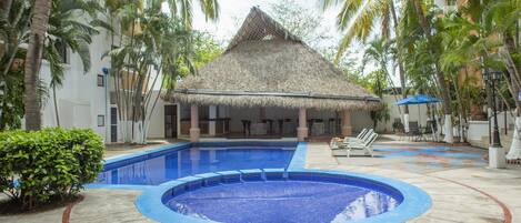 A pool area with a thatched-roof structure, palm trees, and lounge chairs.