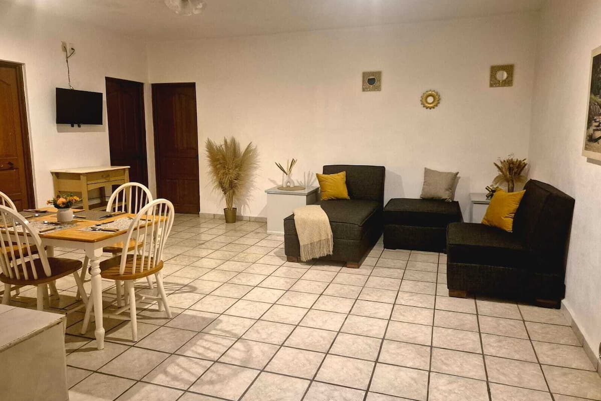 Una sala de estar con comedor, un juego de sofá, un televisor y un ventilador de techo.