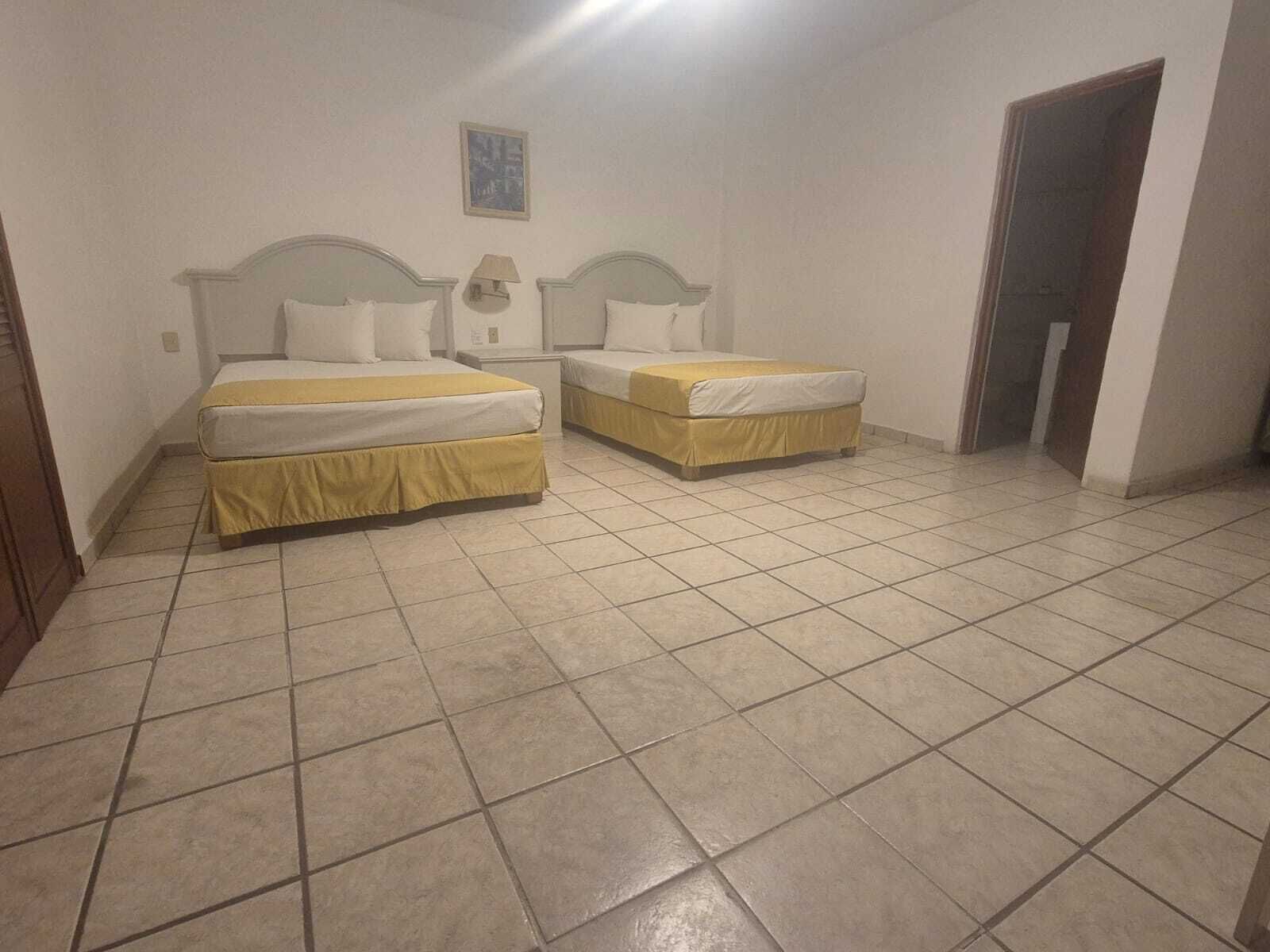 Una habitación con dos camas, una lámpara de pared y una puerta.