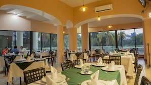 A restaurant with multiple tables set for dining, large windows offering a view of the outdoors, and a modern interior design. - Hotel Costa Brava (Manzanillo)