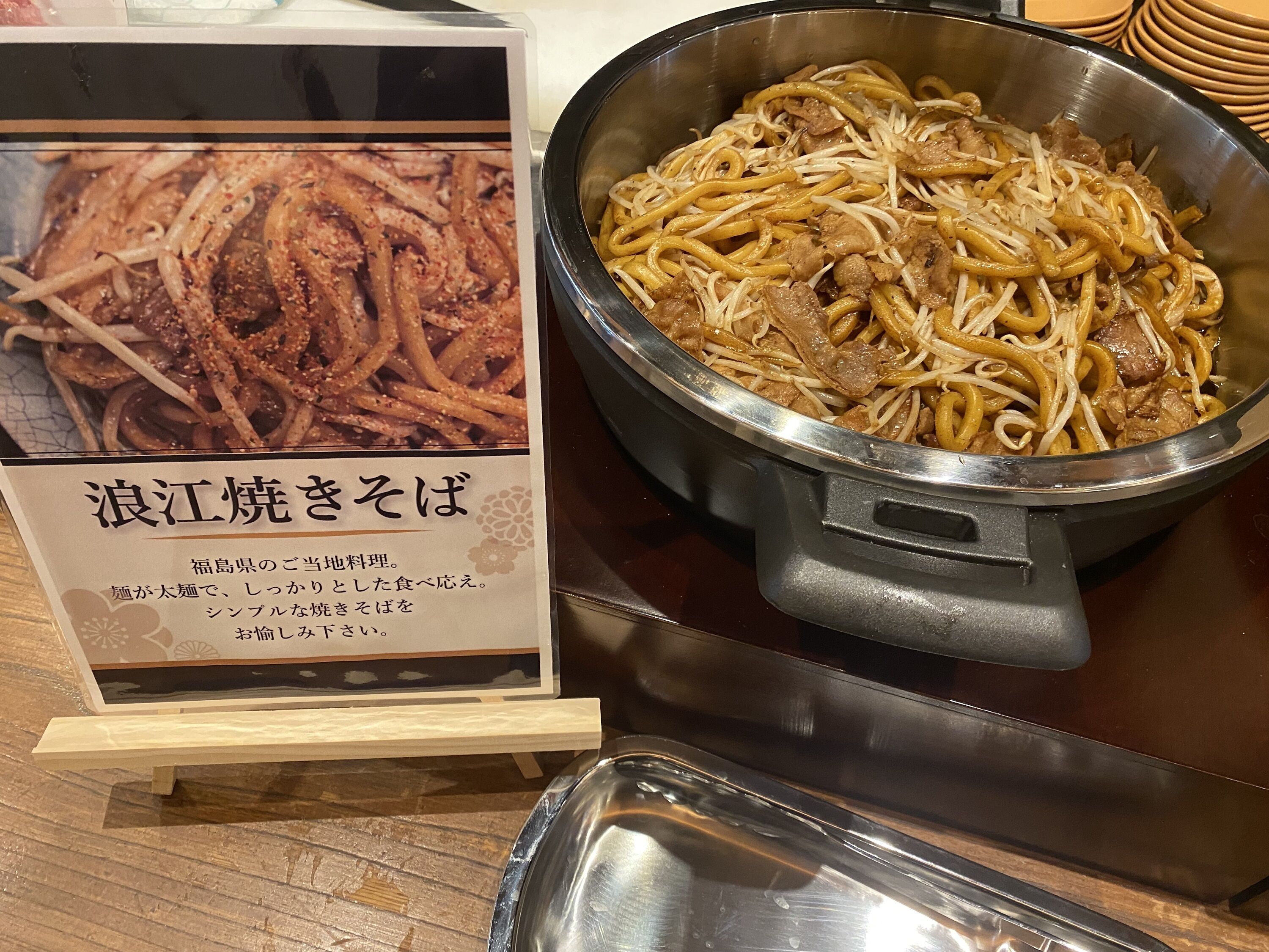 A menu board with a dish description and a pot of noodles with meat and bean sprouts.