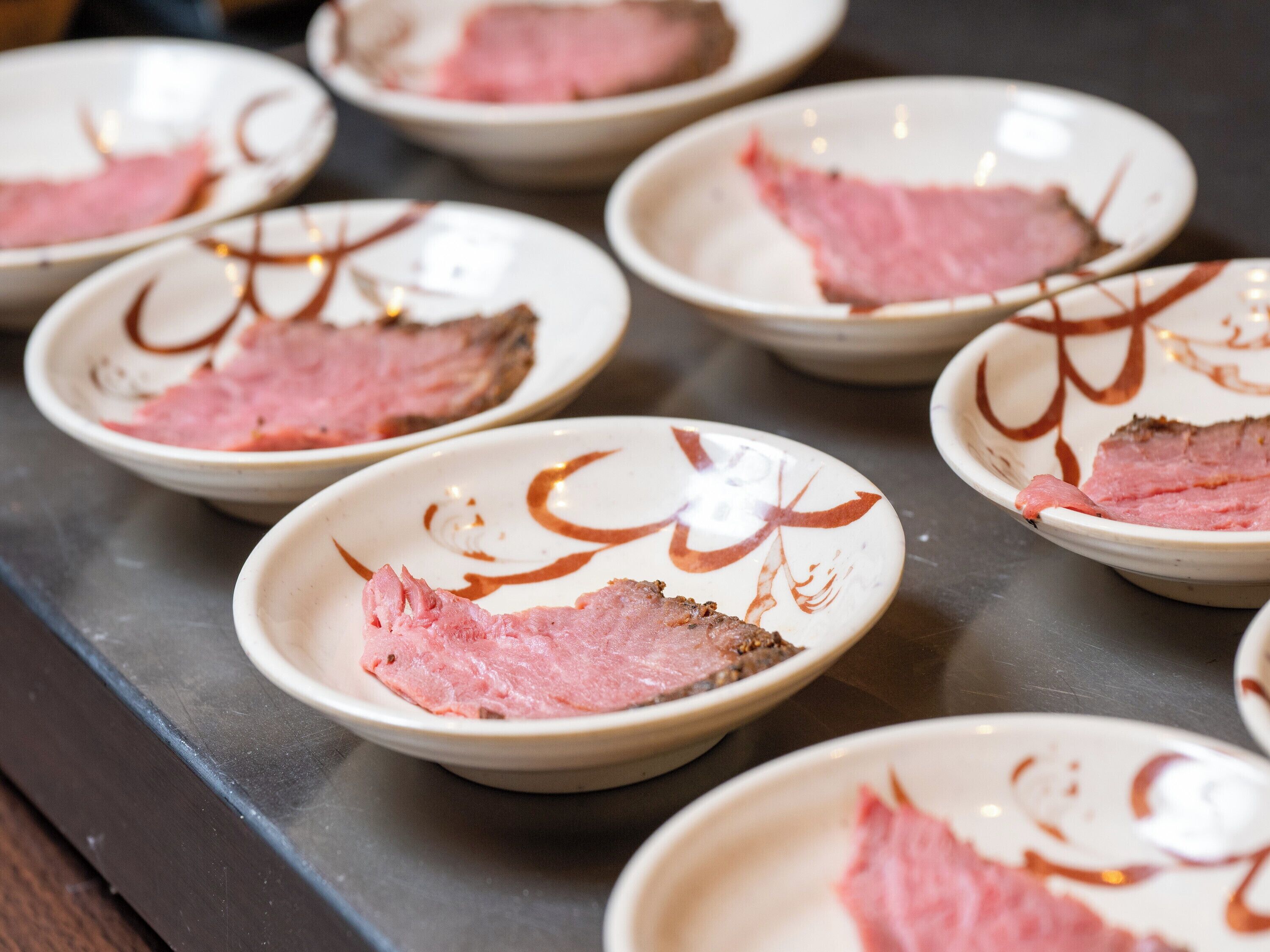 A series of white plates with pink meat slices and chocolate drizzle.