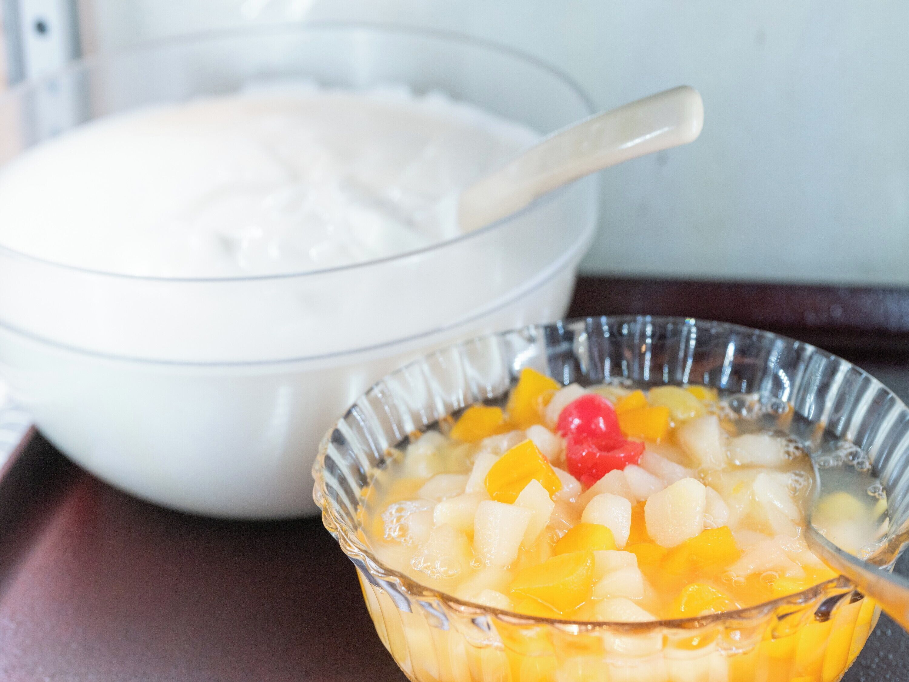 Un tazón de ensalada de frutas con una cuchara y un tazón de yogur.
