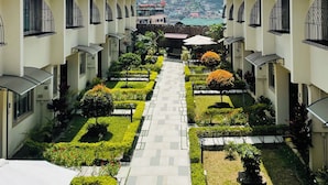 A courtyard with a central pathway flanked by buildings with balconies and a view of a distant town. - Baguio Holiday Villas (Baguio)