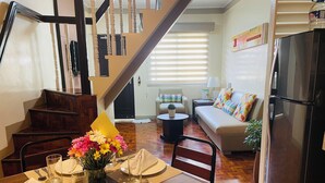 A dining area with a wooden table set for four, a staircase, a living room with a sofa and a coffee table, and a refrigerator. - Baguio Holiday Villas (Baguio)