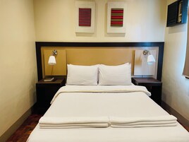A hotel room with a neatly made bed, two bedside tables with lamps, and two wall-mounted air vents.