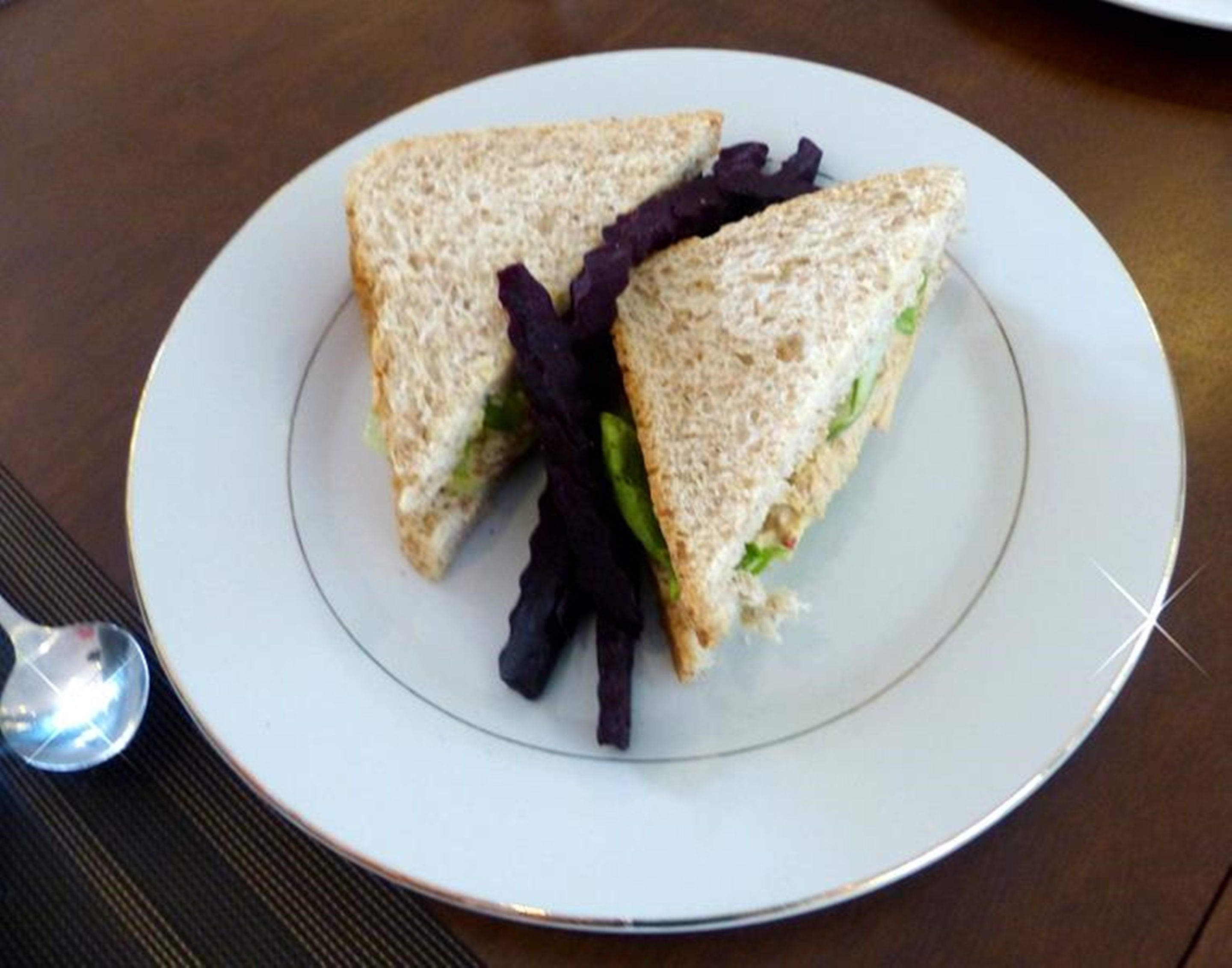Un sándwich sobre un plato blanco, con una cuchara al lado.