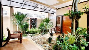 A spacious indoor garden with a variety of plants, a wooden bench, and a decorative elephant sculpture. - Baan Na Khon Hotel (Nakhon Si Thammarat)