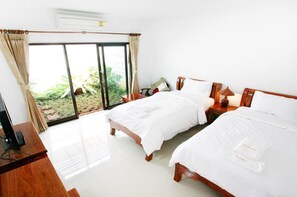 A hotel room with two beds, a desk, a TV, and a large sliding glass door leading to a garden. - Baan Na Khon Hotel (Nakhon Si Thammarat)