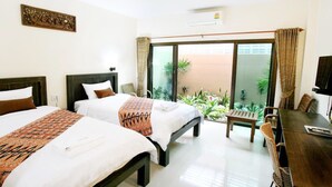 A hotel room with two beds, a dining table, and a view of a garden through a sliding door. - Baan Na Khon Hotel (Nakhon Si Thammarat)